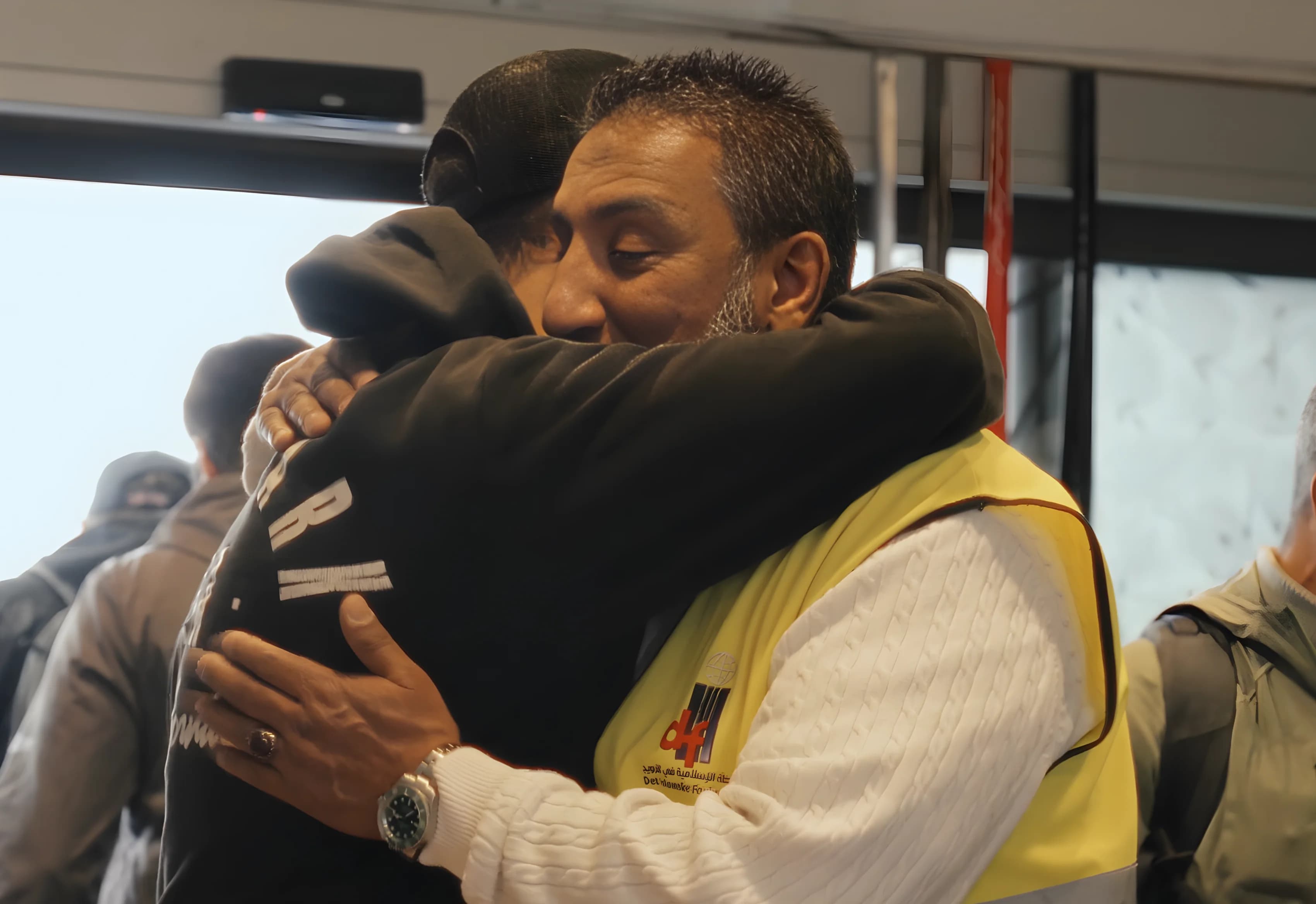 Two men embracing at a Rabita gathering, one wearing a Det Islamske Forbundet volunteer vest